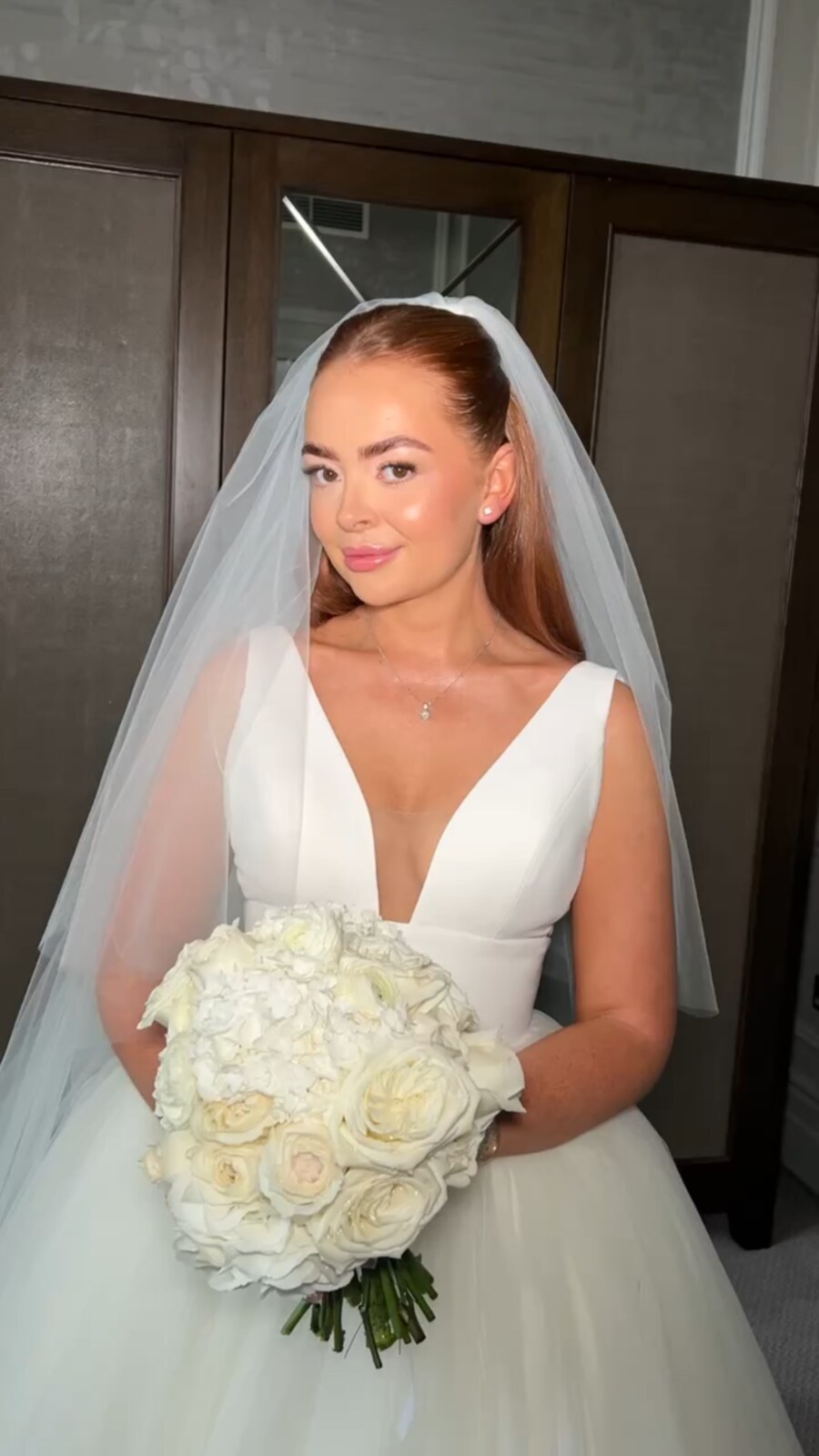 Bride in a veil holding a white bouquet, with polished skin, softly defined eyes and glossy pink lips, with makeup by Abby Christopher